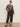 A woman stands confidently with one hand in her pocket, wearing Sanctuary Clothing’s long sleeve perfect mesh tee french kitty extended sizing, paired with cat-eye sunglasses, black wide-leg belted pants, and black flats.