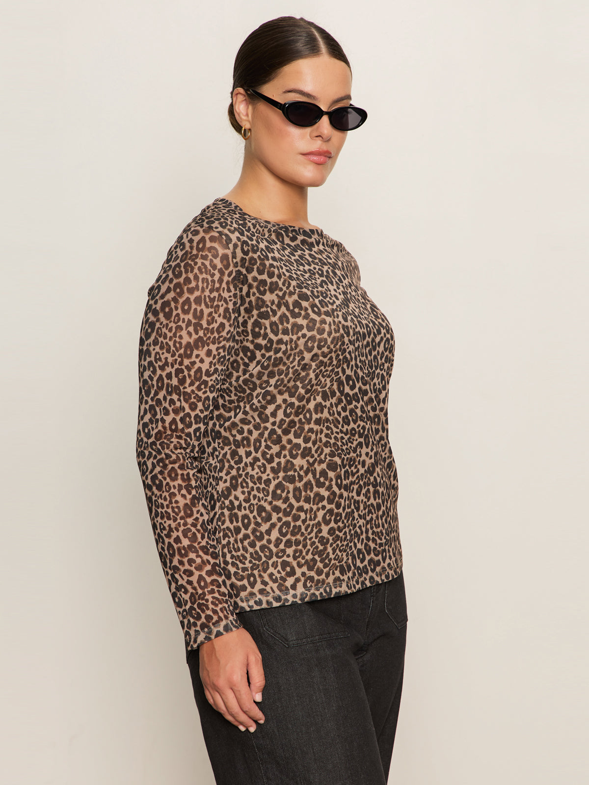 A woman wearing black sunglasses, black pants, and the Sanctuary Clothing long sleeve perfect mesh tee french kitty extended sizing stands against a plain light background, facing slightly to the side.