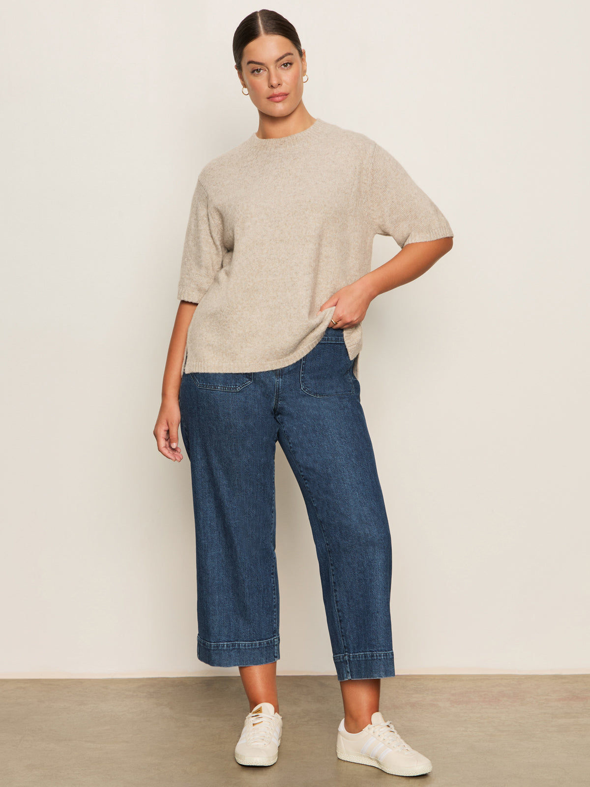 A woman poses casually against a light background wearing the Sanctuary Clothing perfect sweater tee in heather pearl (extended sizing), styled with wide-leg blue jeans and white sneakers. Her hair is pulled back, and one hand rests in her pocket.