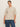 A woman wears the Sanctuary Clothing perfect sweater tee in heather pearl (extended sizing) and blue jeans, standing before a plain light background and looking at the camera with a neutral expression.