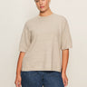 A woman wears the Sanctuary Clothing perfect sweater tee in heather pearl (extended sizing) and blue jeans, standing before a plain light background and looking at the camera with a neutral expression.