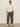A person wearing the Sanctuary Clothing nomad cable popover chalk extended sizing sweater, olive green cargo pants, white sneakers, and black sunglasses stands against a plain white wall with one hand in their pocket.