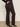 Someone stands against a light background, wearing Sanctuary Clothing's corduroy Hayden bootcut pant in semi sweet (extended sizing) with black heeled ankle boots, one hand in their pocket.