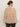 A woman with dark hair in a low bun is seen from behind wearing Sanctuary Clothing’s fade into you ruffle blouse in fawn—a long-sleeve, loose, sheer beige top with a wide back ruffle—paired with dark pants.