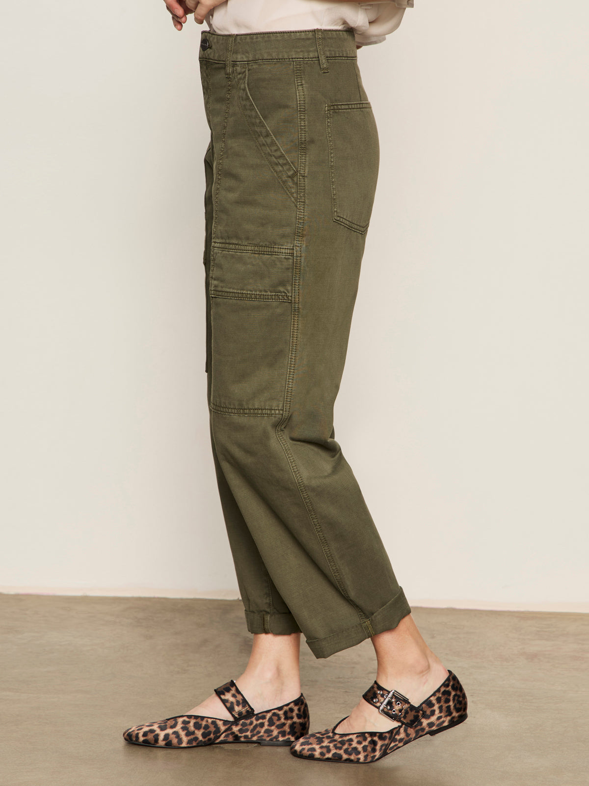 A person stands on a concrete floor, shown from the side, wearing Sanctuary Clothing™s boyfriend utility high rise pant in kalamata and leopard print Mary Jane flats.