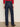 A person stands facing away, wearing Sanctuary Clothing soleil 90s straight jeans indigo dark raw rinse with large back pockets, a red long-sleeve top, and leopard-print flats.