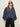 A woman with long light brown hair wears black sunglasses, black pants, and the Sanctuary Clothing personal best blouse in moonshadow. She stands against a plain light background with her hands in her pockets.