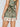 A person wears Sanctuary Clothing's "spring breaker short mezzo sage," a green and beige printed short with intricate floral and paisley patterns. The image highlights the lower back and shorts.