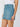 A person wears the all buttoned up skirt dream team by Sanctuary Clothing, a light blue denim mini with front buttons and large pockets, styled with a white sleeveless top and a gold bracelet on their left arm.