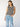 A woman with long brown hair wears the Sanctuary Clothing crochet shell sweater in chalk black stripe, paired with light blue jeans, standing against a plain light background.