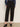 A person models the Sanctuary Clothing ponte barrel trouser in black, paired with a blue long-sleeve shirt and black heeled mules, standing against a plain light background. The waist-up photo excludes the person's face.