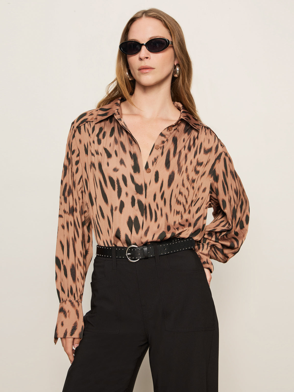 A woman wears Sanctuary Clothing's charter gab barrel pant in black, styled with a brown animal print blouse and black sunglasses, standing against a plain light background.