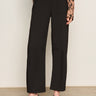 A person wearing Sanctuary Clothing's Charter Gab Barrel Pant in black, styled with a long-sleeve animal print blouse and black heeled mules, stands against a plain background.