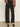 Indoors, a person faces away wearing Sanctuary Clothing's charter gab barrel pant in black, a brown and black patterned long-sleeve blouse, and black open-back block-heeled shoes.