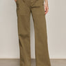 A person wearing Sanctuary Clothing’s cruiser full length pant in dirty martini, featuring wide legs and large front pockets, stands on a gray floor. Only the lower half and their white sneakers are visible.