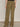 Person wearing Sanctuary Clothing's Cruiser Full Length Pant in Dirty Martini—olive green, flap back pockets with black buttons—standing against a plain light wall. Only the lower back, legs, and part of white shoes are visible.