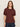 A woman with straight, light brown hair wears the Sanctuary Clothing Shirred Waist Dolman Tee in chicory and dark jeans, standing against a beige background and looking at the camera with a neutral expression.