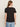 A person with long brown hair is seen from the back against a light background, wearing the Sanctuary Clothing notch neck tee in black and light blue jeans.