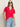 A woman with long brown hair wears the Sanctuary Clothing notch neck tee radiant, light blue jeans, and black oval sunglasses, standing with one hand in her pocket against a neutral background.