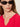 A woman with light skin and long brown hair wears black oval sunglasses, small gold hoop earrings, and the Sanctuary Clothing notch neck tee radiant in red. She looks slightly to the side against a neutral background.