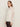 A woman with long brown hair models Sanctuary Clothing's "the ethereal blouse chalk," a sheer white top with ruffled layers and bell sleeves, paired with dark pants, standing sideways against a plain light background.