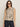 A woman wears the Sanctuary Clothing fuzzy leopard shell mother leo� a sleeveless, beige and black animal print top�paired with dark high-waisted jeans and dark sunglasses, standing against a plain light background.