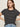 A woman with straight brown hair models the Sanctuary Clothing "the perfect tee white black stripe 5," a black T-shirt with white stripes, paired with light blue jeans, standing hands on hips against a plain light background.