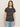 A woman with long brown hair faces forward against a plain background, wearing Sanctuary Clothing’s "the perfect tee white black stripe 5" and light blue jeans. She has a neutral expression.