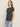 A woman with long, light brown hair wears the Sanctuary Clothing "perfect tee white black stripe 5" and light blue jeans, standing against an off-white background and looking slightly to the side with a neutral expression.