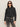 A woman in Sanctuary Clothing’s denim jacket washed black denim and black sunglasses stands against a plain light background, looking forward with a neutral expression.
