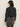 A woman with long brown hair wears black sunglasses and the Sanctuary Clothing denim jacket in washed black denim, paired with faded black jeans, as she stands facing away from the camera against a light-colored wall.