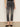 A person wearing Sanctuary Clothing astra kick crop jean in washed black denim, paired with a black top and black slip-on shoes, stands against a plain light-colored wall. The image is cropped to show only the lower half of the body.