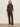 A woman stands against a plain beige wall, wearing the Sanctuary Clothing ls mock essential top semi sweet, matching dark brown belted trousers, and light-colored shoes. She faces forward with a neutral expression.