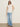 A woman wears Sanctuary Clothing's side tie muscle tee in white with light blue wide-leg jeans, black sandals, and sunglasses, standing against a plain beige background.