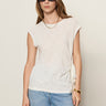 A woman stands against a plain light background wearing Sanctuary Clothing's Side Tie Muscle Tee in white, styled with sunglasses, a gold chain necklace, bracelets, and light blue jeans.