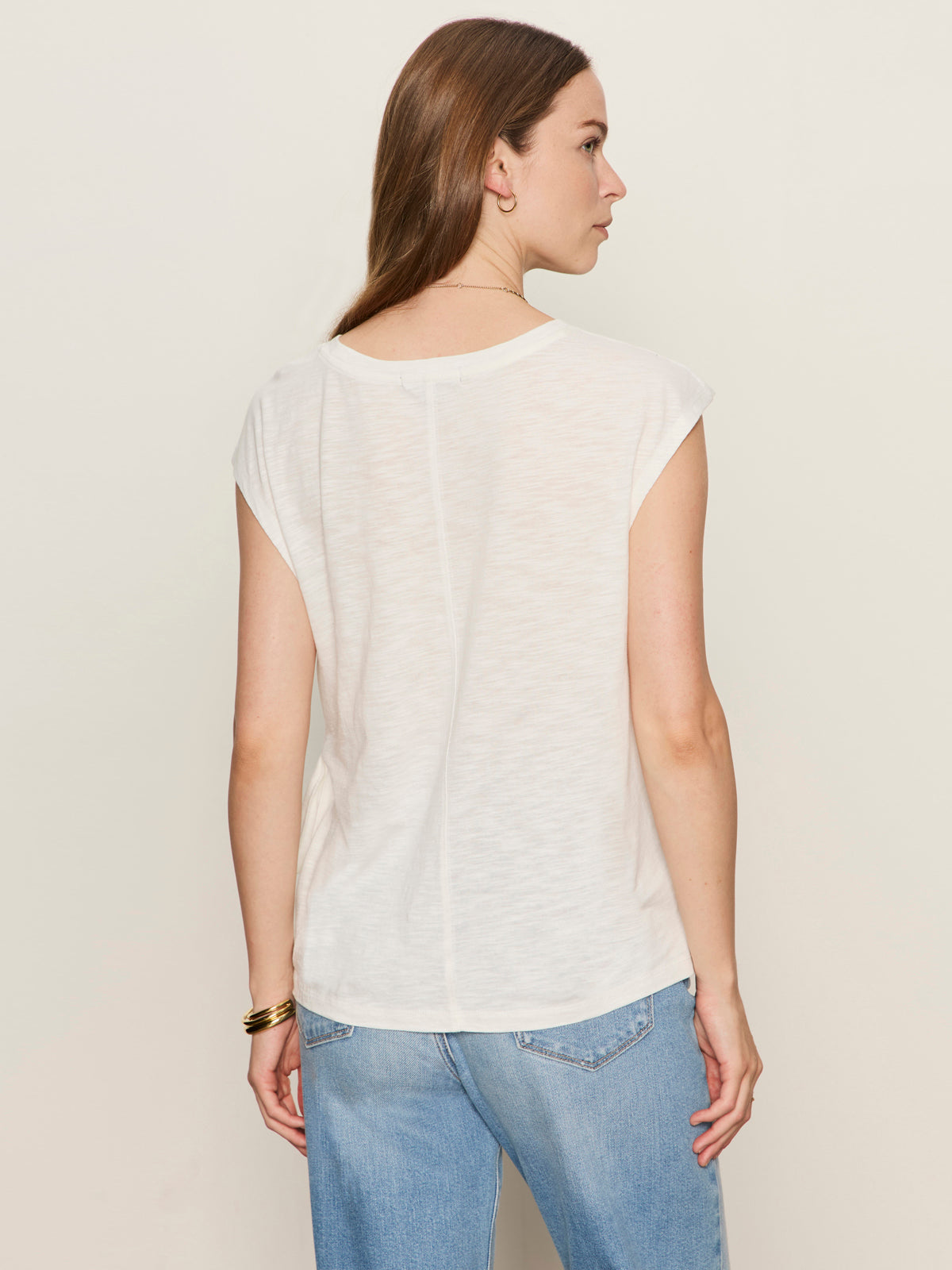 A woman with straight brown hair wears the Sanctuary Clothing side tie muscle tee in white and light blue jeans, standing with her back to the camera against a plain light background.