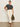 A woman poses confidently in Sanctuary Clothing’s the perfect tee white black stripe 6, paired with high-waisted cream pants, sandals, and an olive green bag against a plain background.
