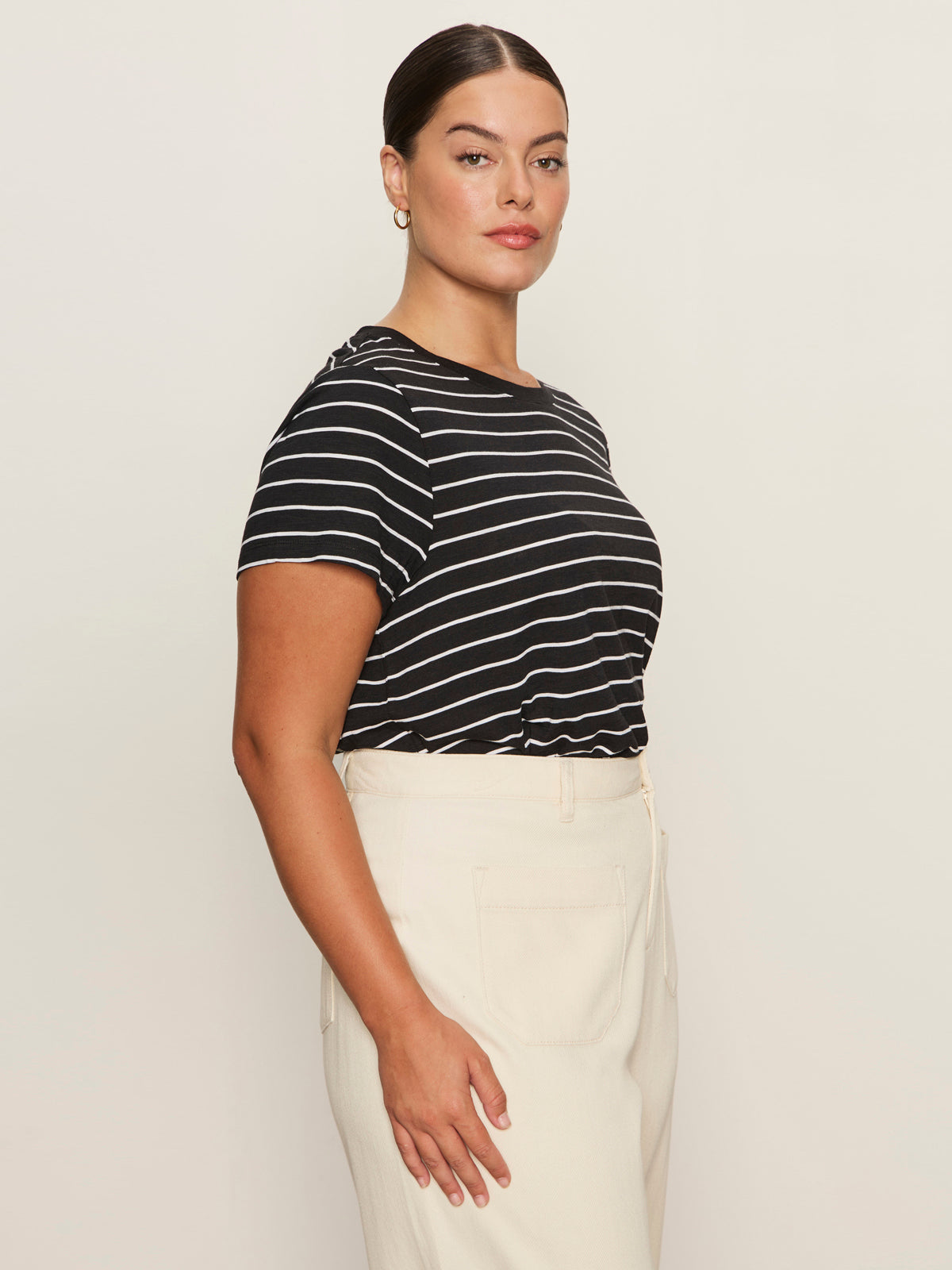 A woman with pulled-back hair and a neutral expression wears Sanctuary Clothing's "the perfect tee white black stripe 6"—a black and white striped short-sleeve shirt—tucked into high-waisted cream pants, standing in profile against a light background.