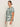 A woman stands sideways against a plain light background wearing Sanctuary Clothing„s œthe perfect tee green oasis extended sizing,� featuring bold green leaf patterns, paired with cream pants and gold hoop earrings.