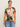A woman with dark hair tied back wears Sanctuary Clothing's "the perfect tee reef vibes extended sizing" in a floral pink, green, and orange print with gold hoop earrings and blue jeans, standing against a plain off-white background.
