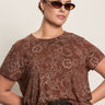 A woman wearing Sanctuary Clothing’s the perfect tee boheme extended sizing stands against a plain light background with her hand on her hip, sunglasses on, and dark high-waisted pants.
