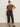 A woman wears Sanctuary Clothing's the marine jeans after hours extended sizing with sunglasses, a brown patterned short-sleeve top, and black flats, standing against a plain light wall with one hand on her hip.