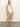 A person with long hair wears the "Refresh Rib V Wire Mio White" swimsuit by Sanctuary Clothing. They're barefoot on a smooth, neutral floor against a plain backdrop.