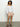 A person with curly hair is wearing a ballet tie top white from Sanctuary Clothing, paired with beige shorts on a gray floor against a light background. They complete the look with brown sandals.