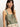 Someone with long hair wears the "button back cami mezzo sage" by Sanctuary Clothing, featuring an intricate floral pattern. They accessorize with hoop earrings and layered necklaces, looking slightly to the side against a plain light background.