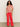 A woman with curly hair wears the Sanctuary Clothing relaxed vacation shirt sunny riviera, styled with bright red wide-leg pants and brown sandals, standing against a plain light background.