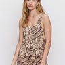 A woman with long blonde hair wears the Sanctuary Clothing desert tank and desert bandana pants, featuring a beige and dark brown paisley pattern, standing against a plain light background with a neutral expression.