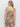 A woman with blonde hair models the Sanctuary Clothing desert tank desert bandana, a sleeveless beige jumpsuit with a brown paisley pattern, tie waist, and wide straps. She is shown from the back against a plain white background.