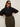 A woman wearing dark sunglasses and the Sanctuary Clothing petal drop blouse black extended sizing stands with her hands on her hips, paired with high-waisted olive green pants against a plain light background.