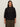 A woman with long brown hair models the Sanctuary Clothing petal drop blouse in black (extended sizing), a loose-fitting, eyelet button-up with three-quarter sleeves, paired with olive green pants against a neutral background.